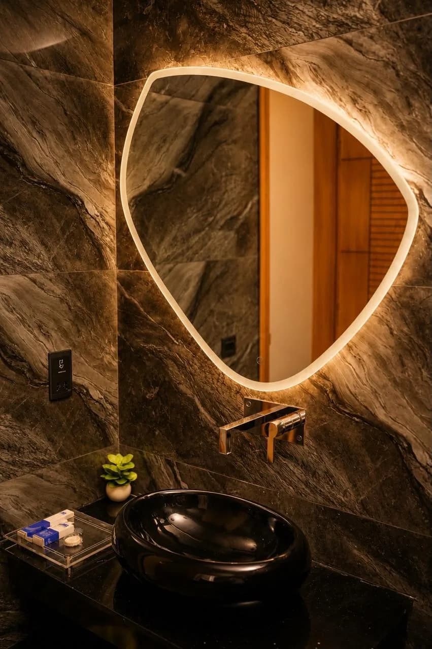 Bathroom finished in dark marble with a backlit organic mirror and black stone basin