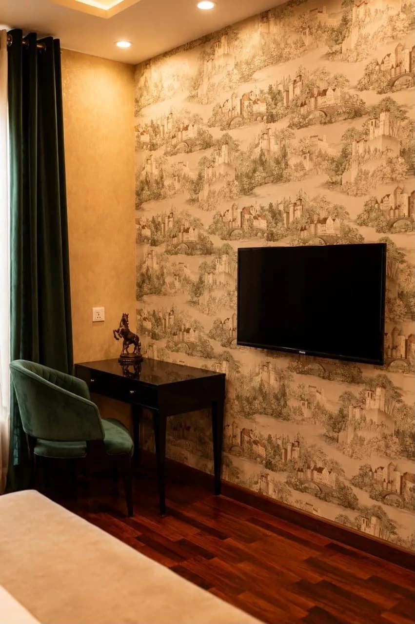 Writing desk against toile wallpaper with a green velvet chair and wall-mounted television