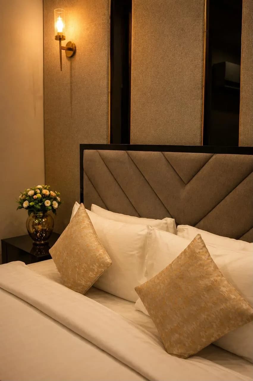 Royale Suite bed dressed in white linen with gold cushions and a brass reading light